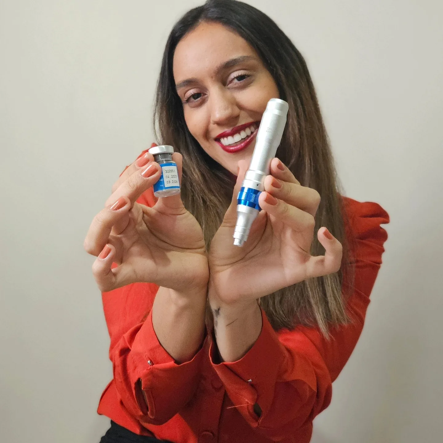 Thayane sorrindo largo, com a ampola numa mão e a caneta de microagulhamento erguida na outra