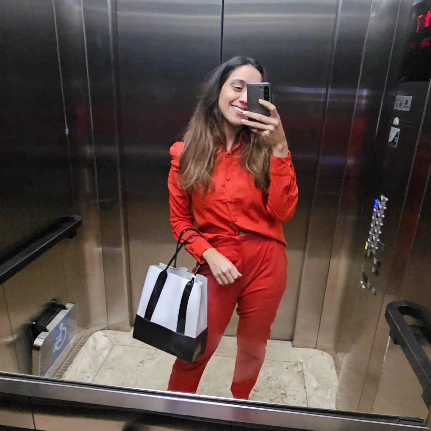 Thayane de macacão vermelho fotografando-se no espelho do elevador