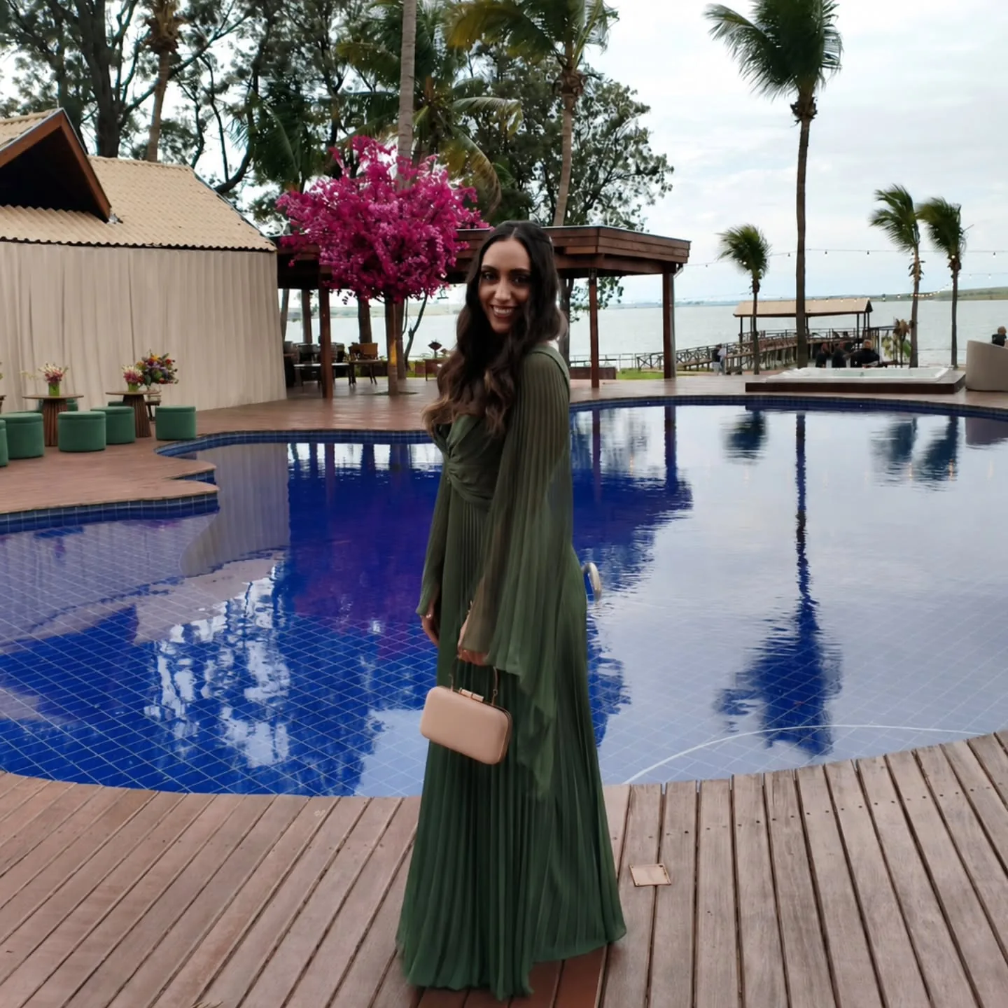 Thayane de vestido verde longo junto à piscina ao entardecer