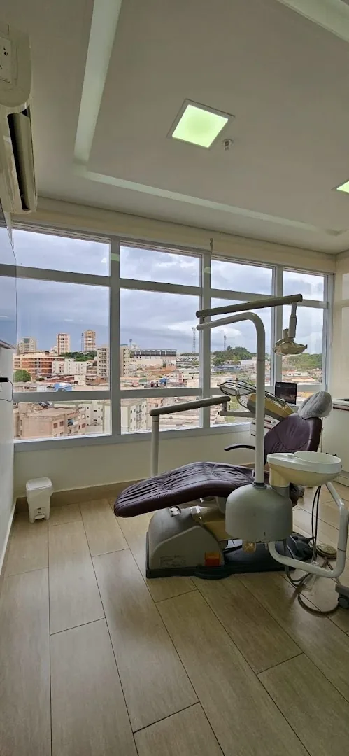 Sala com cadeira odontológica junto a uma janela ampla com vista da cidade